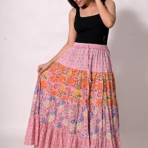 Può includere: Gonna lunga a balze con stampa floreale nei toni del rosa, arancione e blu. La gonna ha un punto vita con coulisse e uno stile bohémien fluido. La modella indossa una canotta nera. La gonna è un capo d'abbigliamento vivace.