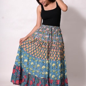 Puede incluir: Una falda larga escalonada con estampado floral en tonos azules, rosas y amarillos. La falda tiene un dobladillo con volantes y se combina con una camiseta sin mangas negra. El diseño de la falda presenta un patrón floral repetido.