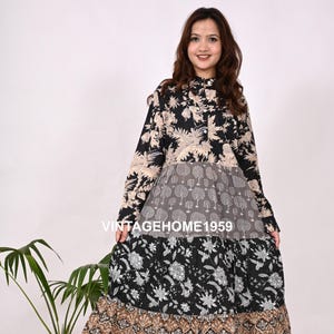 May include: A long, tiered dress with a floral and geometric pattern in black, beige, and gray. The dress has long sleeves and a high collar. The text "VINTAGEHOME1959" is visible on the dress. The dress is worn with sandals.