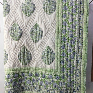 May include: A white cotton quilt with a green and blue floral pattern. The quilt is quilted in a diamond pattern and has a border of green and blue floral fabric.