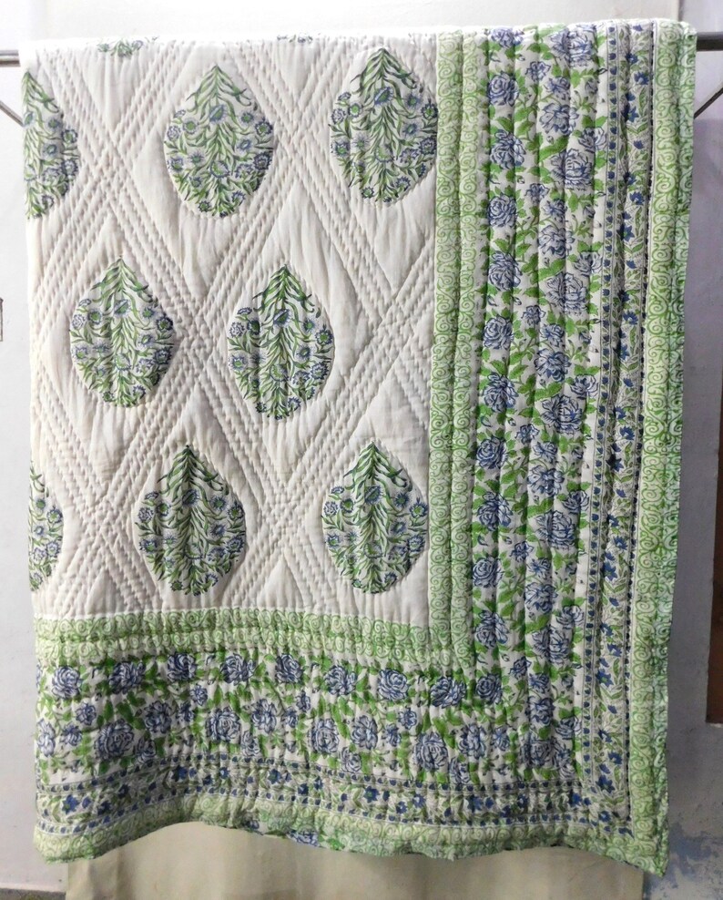 May include: A white cotton quilt with a green and blue floral pattern. The quilt is quilted in a diamond pattern and has a border of green and blue floral fabric.