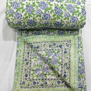 May include: A white cotton quilt with a floral pattern in shades of blue and green. The quilt is folded in half and has a border of green and white.