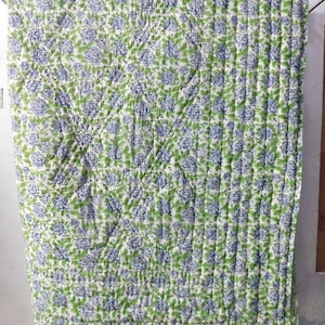 May include: A white cotton quilt with a blue and green floral pattern. The quilt is quilted in a diamond pattern and has a white border.