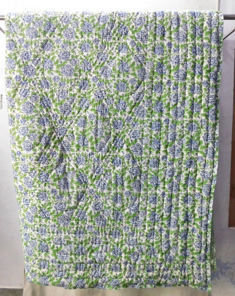 May include: A white cotton quilt with a blue and green floral pattern. The quilt is quilted in a diamond pattern and has a white border.