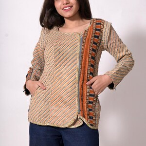 May include: Beige and orange patterned jacket with a full-length zipper. The jacket has long sleeves and pockets. The design includes a vertical stripe of orange, black, and blue. The model is wearing blue jeans.