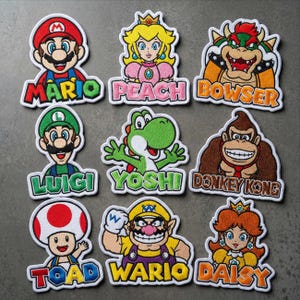 May include: Nine colorful embroidered patches featuring characters from the Super Mario video game series. Characters include Mario, Peach, Bowser, Luigi, Yoshi, Donkey Kong, Toad, Wario, and Daisy. Each patch has a white border and the character's name.