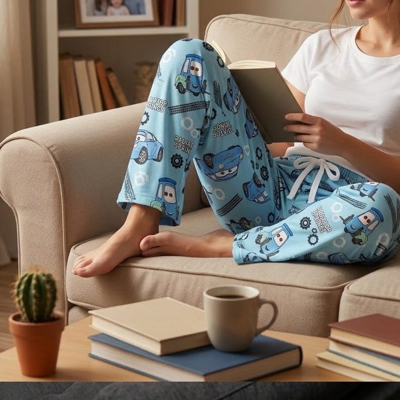 May include: Light blue pajama pants featuring a repeating pattern of cartoon cars, tire tracks, and gear icons, with the text Radiator Springs printed throughout. The pants include a white drawstring waistband and a relaxed, loose-fitting leg design.