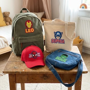 May include: An assortment of children's accessories, including a green backpack, a red baseball cap, a beige tote bag, and a denim crossbody bag. Each item features a superhero-themed patch with a name. The backpack has an Iron Man patch and the name "LEO".