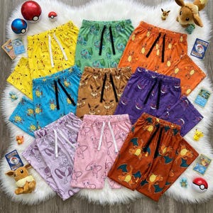 May include: A collection of nine pairs of lounge pants featuring various Pokemon characters including Pikachu, Bulbasaur, Charmander, Squirtle, Eevee, Gengar, Mewtwo, Mew, and Charizard, each with a drawstring waistband and a repeating character print.