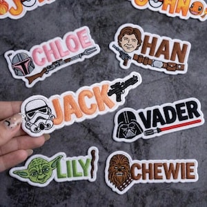 May include: Embroidered patches featuring Star Wars characters and names, including "Chloe," "Han," "Jack," "Vader," "Lily," and "Chewie." Each patch showcases a character image and name in a colorful, detailed design.