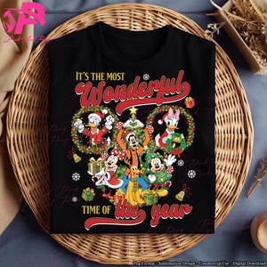 Könnte beinhalten: Schwarzes T-Shirt mit einem Weihnachtsdesign mit Disney-Figuren. Donald Duck, Goofy, Mickey und Minnie Mouse sowie Daisy Duck sind von Kränzen und Geschenken umgeben. Der Text lautet "It's the Most Wonderful Time of the Year."
