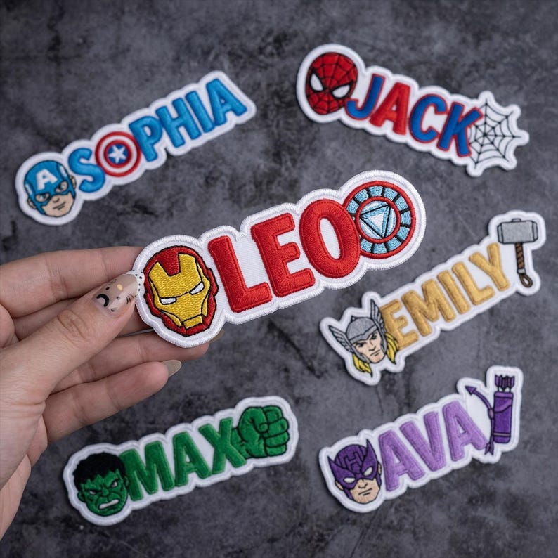 May include: Embroidered patches featuring superhero-themed designs and names. The patches include characters like Captain America, Spider-Man, Iron Man, Hulk, Thor, and Hawkeye, with names such as Sophia, Jack, Leo, Emily, Max, and Ava.