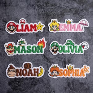 May include: Embroidered name patches featuring characters from a popular video game. Each patch has a different name in a colorful font, with matching character illustrations. The patches include names like Liam, Emma, Mason, Olivia, Noah, and Sophia.