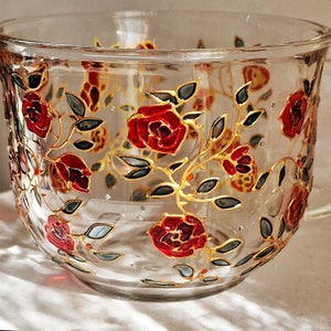 May include: A clear glass mug featuring a hand-painted design of red roses and gold vines. The roses are painted in a realistic style with red and gold accents.