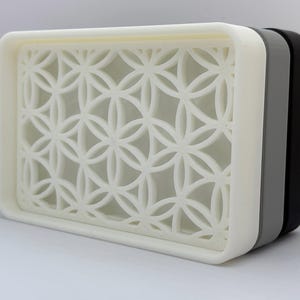 K&ouml;nnte beinhalten: Ein wei&szlig;er Seifenspender aus Kunststoff mit geometrischem Muster. Der Spender hat eine graue und schwarze Basis.