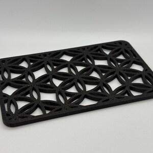 K&ouml;nnte beinhalten: Schwarzer Untersetzer mit geometrischem Design und einem sich wiederholenden Muster aus Kreisen und Ovalen. Der Untersetzer ist aus einem dicken, strapazierf&auml;higen Material gefertigt.