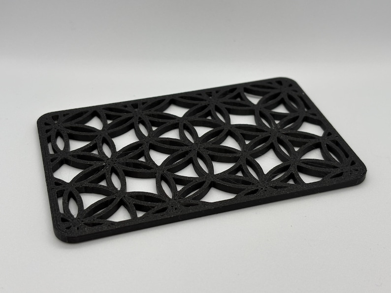 K&ouml;nnte beinhalten: Schwarzer Untersetzer mit geometrischem Design und einem sich wiederholenden Muster aus Kreisen und Ovalen. Der Untersetzer ist aus einem dicken, strapazierf&auml;higen Material gefertigt.