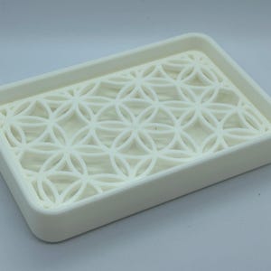 K&ouml;nnte beinhalten: Wei&szlig;e Seifenablage aus Kunststoff mit geometrischem Muster. Die Ablage ist so konzipiert, dass Wasser ablaufen kann.