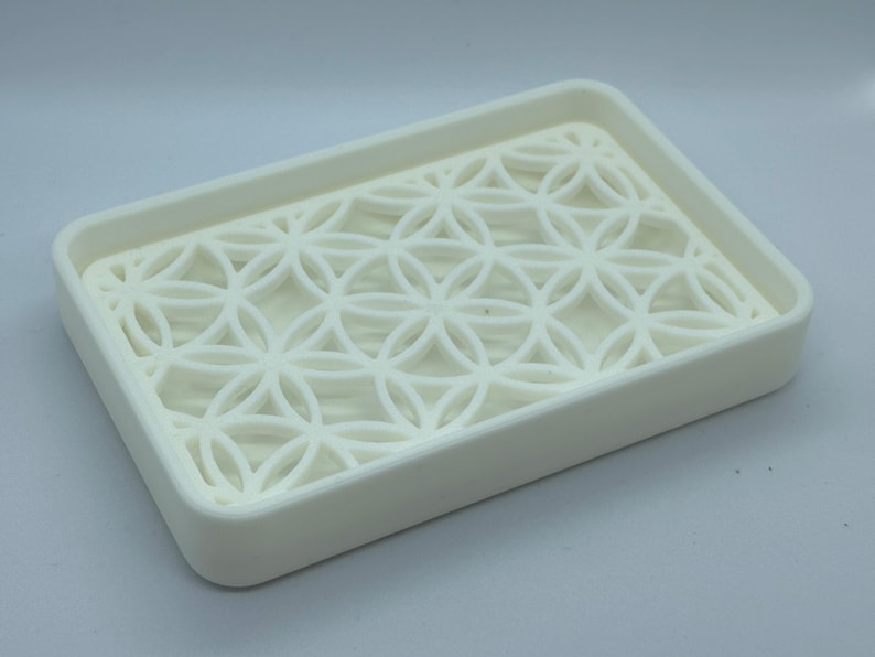 K&ouml;nnte beinhalten: Wei&szlig;e Seifenablage aus Kunststoff mit geometrischem Muster. Die Ablage ist so konzipiert, dass Wasser ablaufen kann.