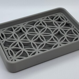 K&ouml;nnte beinhalten: Eine graue Seifenschale mit geometrischem Muster. Die Schale ist aus Kunststoff und hat einen erh&ouml;hten Rand, damit die Seife nicht verrutscht.