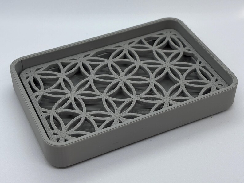 K&ouml;nnte beinhalten: Eine graue Seifenschale mit geometrischem Muster. Die Schale ist aus Kunststoff und hat einen erh&ouml;hten Rand, damit die Seife nicht verrutscht.