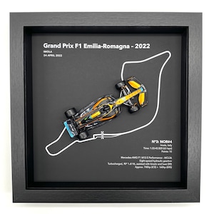 May include: A framed black and white illustration of a race track with a miniature black and gold race car on the track. The text "Grand Prix F1 Emilia-Romagna - 2022" is at the top of the frame. The text "N°3: NOR#4" is at the bottom of the frame.