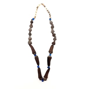 Puede incluir: Un collar marrón y azul hecho de cuentas de madera y vidrio. El collar está hecho de una cadena de cuentas de madera marrón con cuentas de vidrio azul intercaladas.