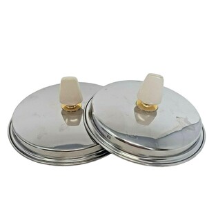 Puede incluir: Dos tapas de olla plateadas con pomos blancos y detalles dorados.