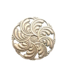 May include: A silver-toned metal decorative button with a circular design featuring intricate swirls and a central hexagon.