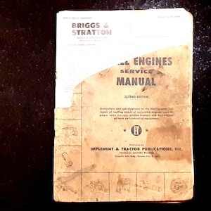 May include: A vintage Briggs & Stratton air cooled engines service manual, second edition, published by Implement & Tractor Publications, Inc. The cover is tan with dark text, showing significant wear, staining, and a torn upper right corner.