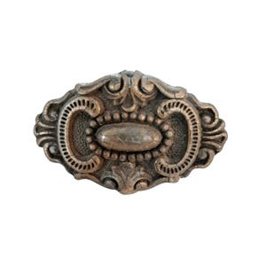 Puede incluir: Un tirador de cajón o pomo de armario de forma ovalada con un acabado en bronce metálico. La pieza presenta un intrincado patrón en relieve con detalles de volutas, un elemento ovalado central liso y un borde texturizado con pequeños acentos.