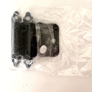 Puede incluir: Bisagra de armario negra con mecanismo de cierre automático. La bisagra está en una bolsa de plástico transparente.