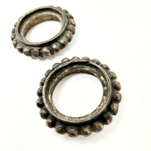 May include: Two circular metal components with a dark, tarnished finish. Each piece features a raised, beaded outer edge surrounding a smooth, recessed center opening. The metal has a weathered, aged appearance with visible texture and patina.