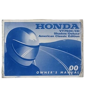 Può includere: Manuale del proprietario Honda VT750C/CD Shadow/Deluxe American Classic Edition blu e bianco. La copertina presenta un motociclista con casco e una grafica stradale. Il manuale è contrassegnato "00".