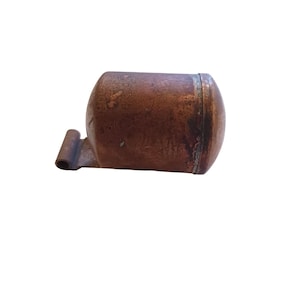 May include: A copper-coloured metal object with a rounded top and a small, flat, rectangular tab extending from the side. The object has a slightly worn, aged appearance.