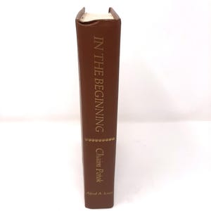 May include: A brown hardcover book titled "IN THE BEGINNING" with gold lettering. The author's name, Chaim Potok, is also in gold. The book has a decorative gold band and the publisher's name, Alfred A. Knopf, is at the bottom.