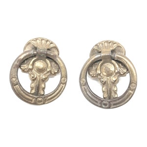 May include: Two antique brass drawer pulls with a ring design and ornate floral details.