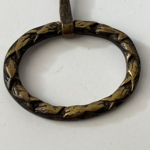 May include: A close-up of a brass oval ring with a decorative design of leaves around the edge.
