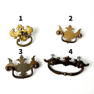 Puede incluir: Cuatro tiradores de cajón de latón numerados del 1 al 4. Cada tirador cuenta con una placa decorativa y un asa oscilante. El metal tiene un acabado dorado desgastado con diversas formas y tamaños ornamentados, incluyendo uno con tornillos.