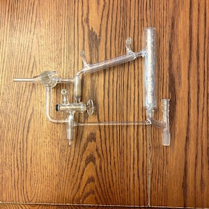 May include: A glass laboratory apparatus with multiple tubes and valves. The apparatus is made of clear glass and has a silver-colored valve.