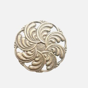 May include: A circular metal button with an antique brass finish, featuring a raised, swirling leaf-like pattern radiating from a central octagonal point. The design includes openwork spaces between the curved, textured metallic elements.