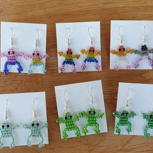 May include: Six pairs of beaded frog earrings, each pair featuring a different colour combination. The colours include rainbow, pink, blue, grey, and green.