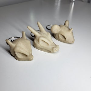 Könnte beinhalten: Drei beigefarbene Schlüsselanhänger in Form von Tierschädeln. Die Schlüsselanhänger sind aus glattem, mattem Material gefertigt und haben ein schlichtes, minimalistisches Design.