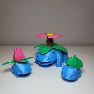 Peut inclure: Trois figurines Pokémon imprimées en 3D de couleur bleue et verte. La plus grande figurine est un Bulbizarre bleu avec une fleur rose sur la tête. Les deux autres figurines sont plus petites et ont des feuilles vertes sur la tête.