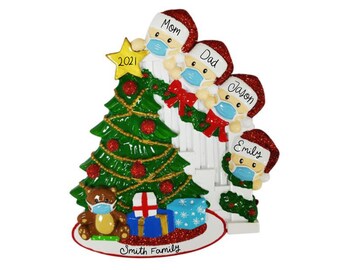May include: A white Christmas ornament featuring a family of five wearing Santa hats and face masks. The family is standing in front of a decorated Christmas tree with a star on top. The ornament also includes a teddy bear wearing a face mask and a gift box. The text "Smith Family" is written on the base of the ornament.