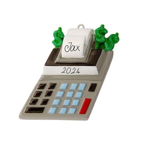May include: A gray and white calculator ornament with green dollar signs and the word "Tax" on the top. The calculator has a red button and the year "2024" printed on the front.