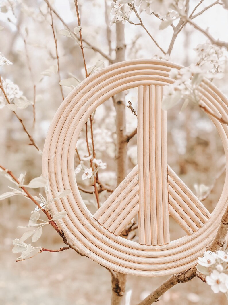 K&ouml;nnte beinhalten: Ein Wanddekor aus Naturholz in Form eines Friedenszeichens mit geflochtenem Design. Das Friedenszeichen h&auml;ngt an einem Baumzweig mit wei&szlig;en Bl&uuml;ten.