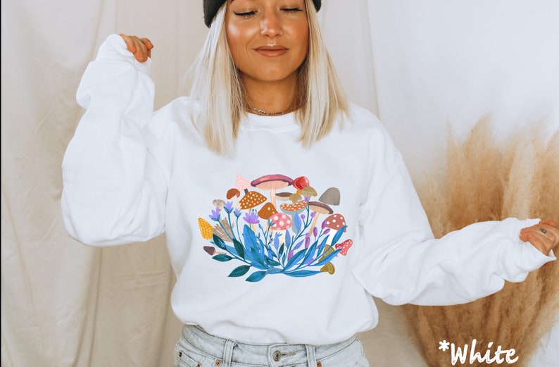 May include: White long-sleeved sweatshirt with a colourful mushroom and floral graphic print. The text "*White" is visible in the bottom right corner of the image.