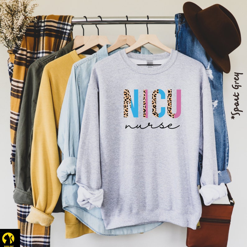 May include: A gray sweatshirt with a graphic design that says "NICU nurse" in blue, pink, and leopard print letters.