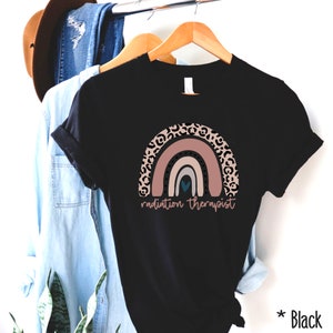 Puede incluir: Camiseta negra con un dise&ntilde;o de arco&iacute;ris con un borde de estampado de leopardo y el texto "radiation therapist".